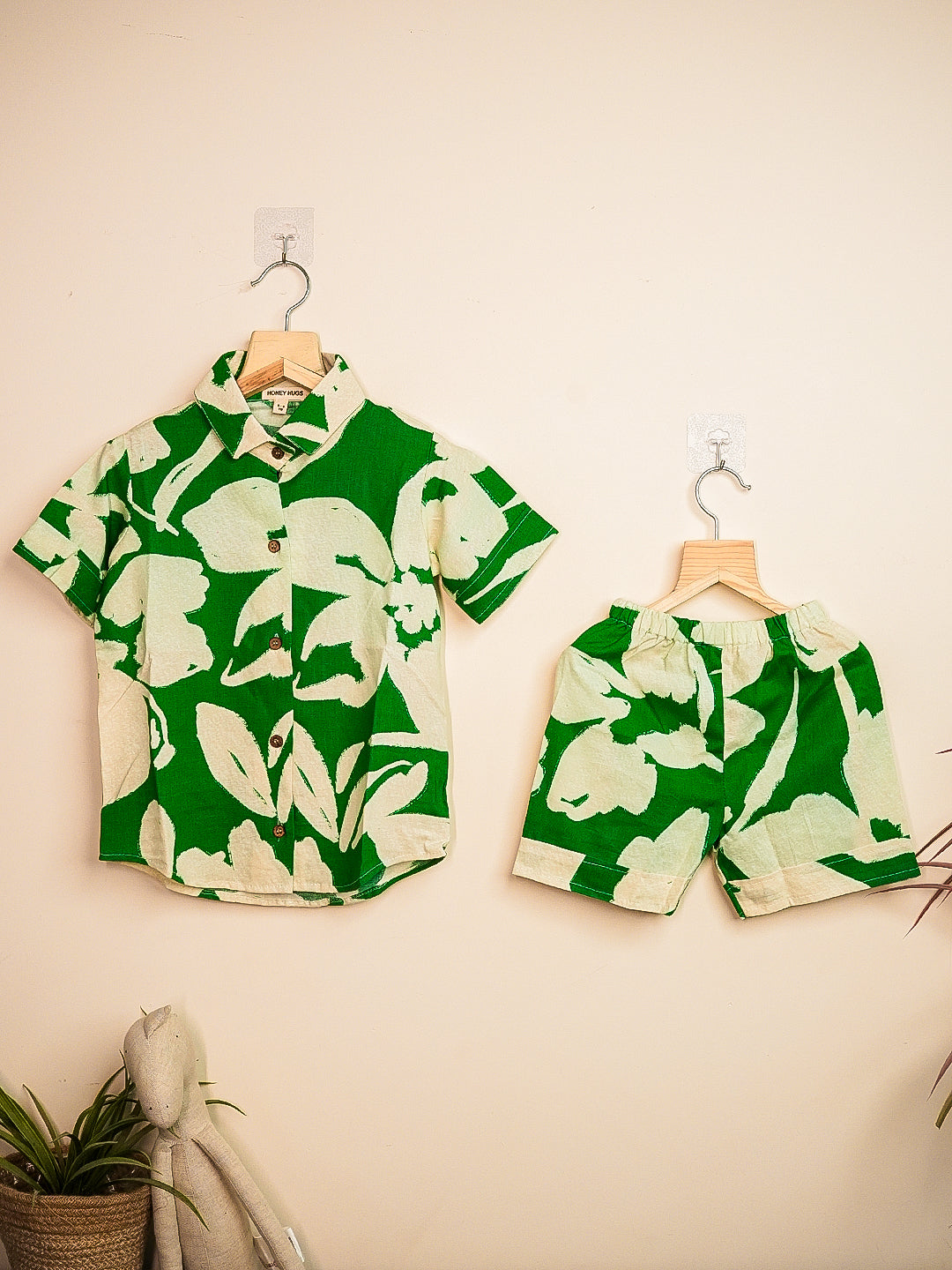 Green and white floral shirt and shorts set hanging on a beige wall.