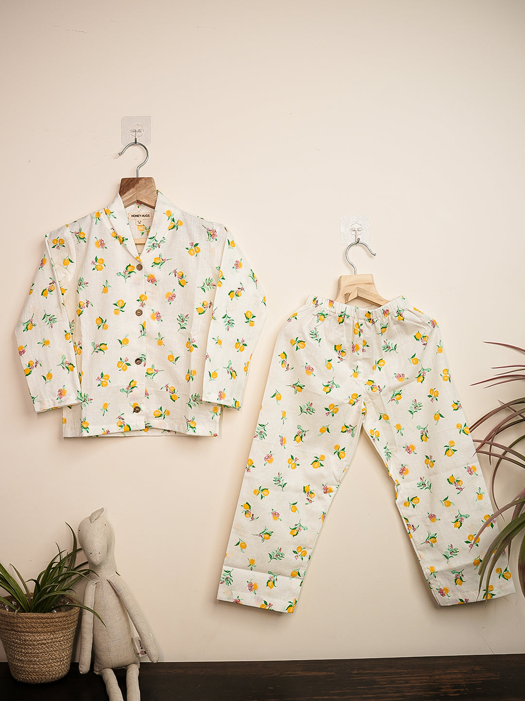 Children's pajama set with floral pattern on hangers against a beige wall.