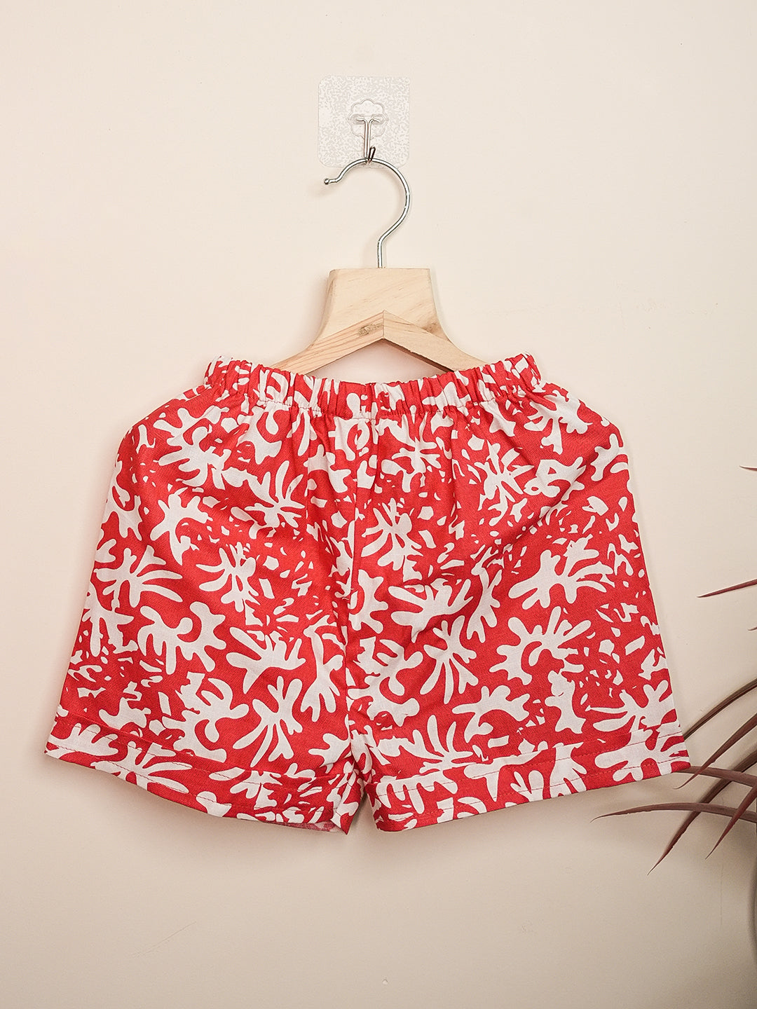 Red shorts with white floral pattern on a hanger against a beige background