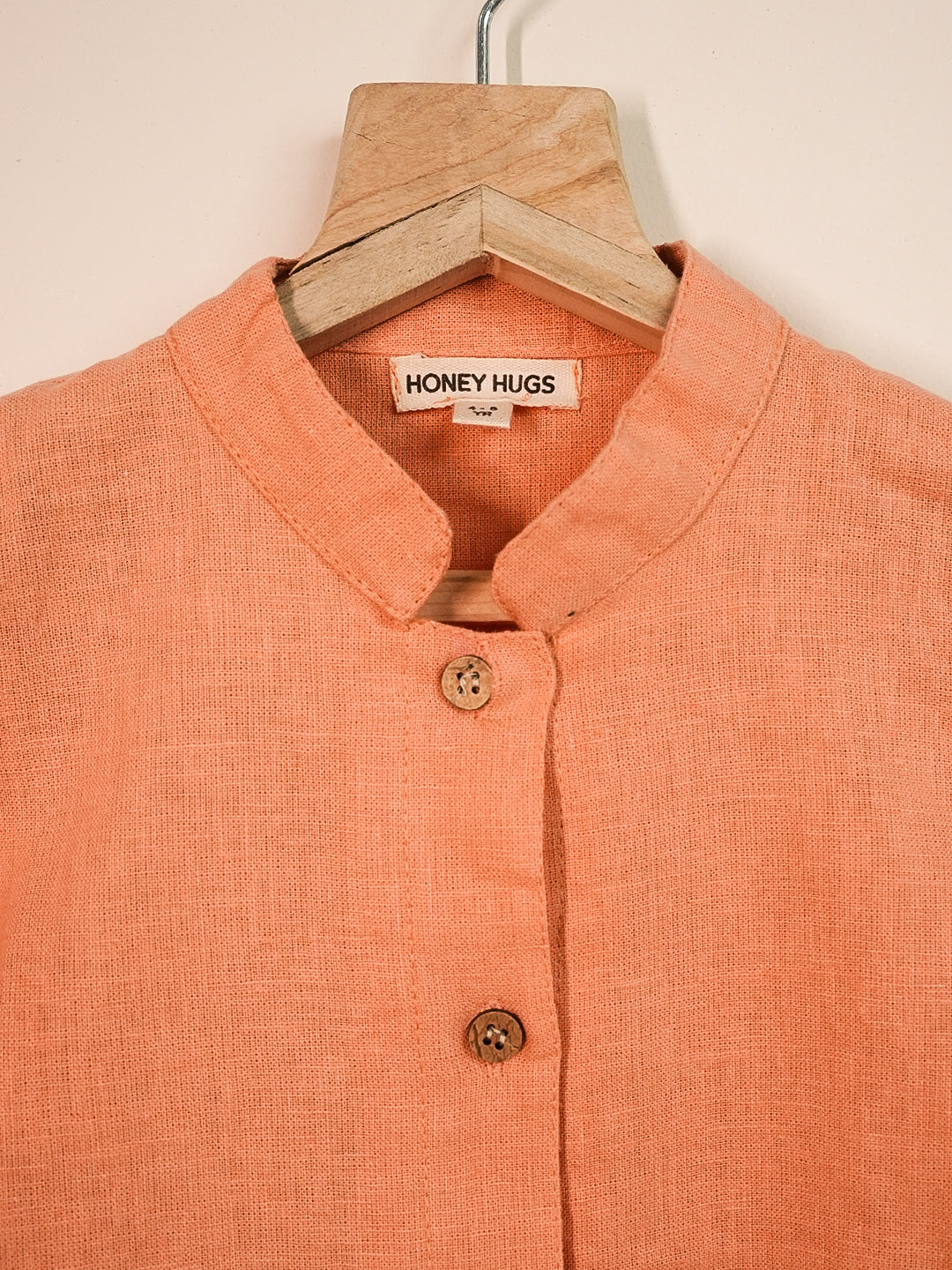 Orange shirt with 'Honey Hugs' label on a wooden hanger against a beige background