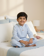 Child wearing blue pajamas sitting on a bed in a bedroom setting
