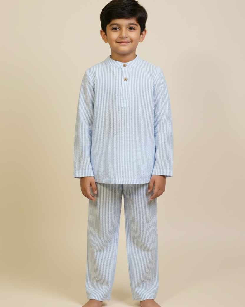 Young boy wearing a light blue striped kurta with white pants on a beige background