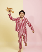 Child wearing red and white striped pajamas holding a wooden airplane on a two-tone yellow and pink background