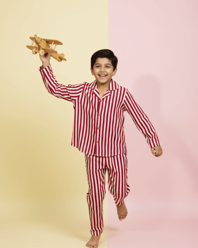 Child wearing red and white striped pajamas holding a wooden airplane on a two-tone yellow and pink background