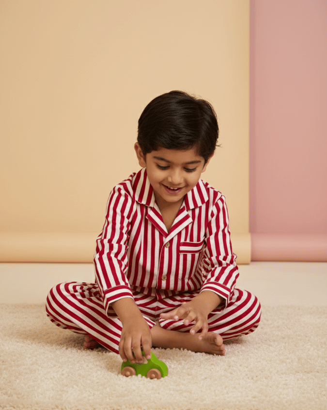Child in red and white striped pajamas playing with a green toy on a beige floor.