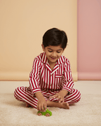 Child in red and white striped pajamas playing with a green toy on a beige floor.