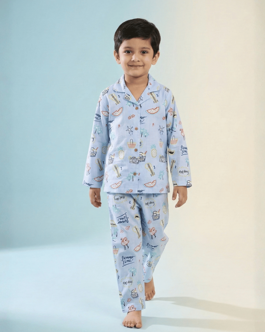 Smiling young boy wearing light blue printed pajamas, walking barefoot on a pastel background.