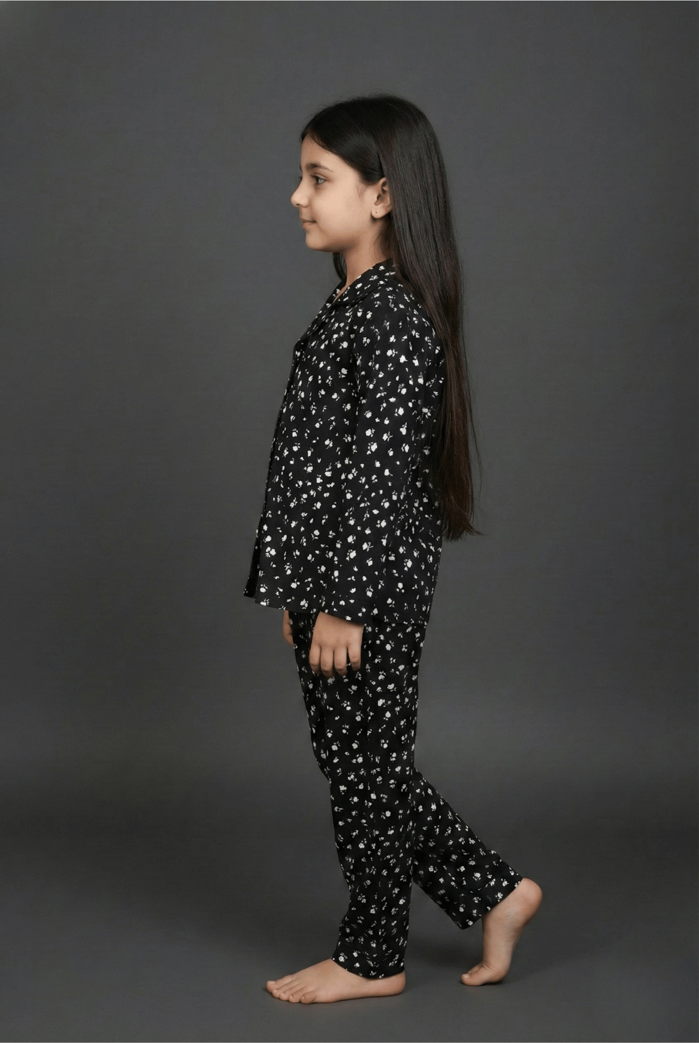 Young girl wearing a black pajama set with white patterns on a gray background