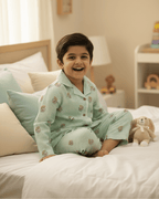 Child wearing a light green pajama set with teddy bear pattern on a bed.