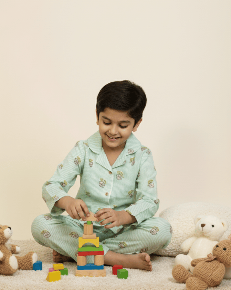 Child playing with building blocks wearing light green pajamas with animal prints, surrounded by teddy bears on a beige background.