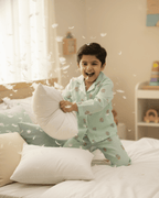 Child in pajamas playing with pillows on a bed in a bright room