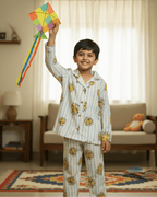 Child in a patterned outfit holding a colorful kite indoors.