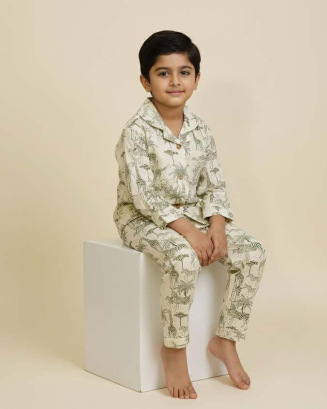 Cute boy sitting on a white cube wearing giraffe and palm-tree print pajamas.